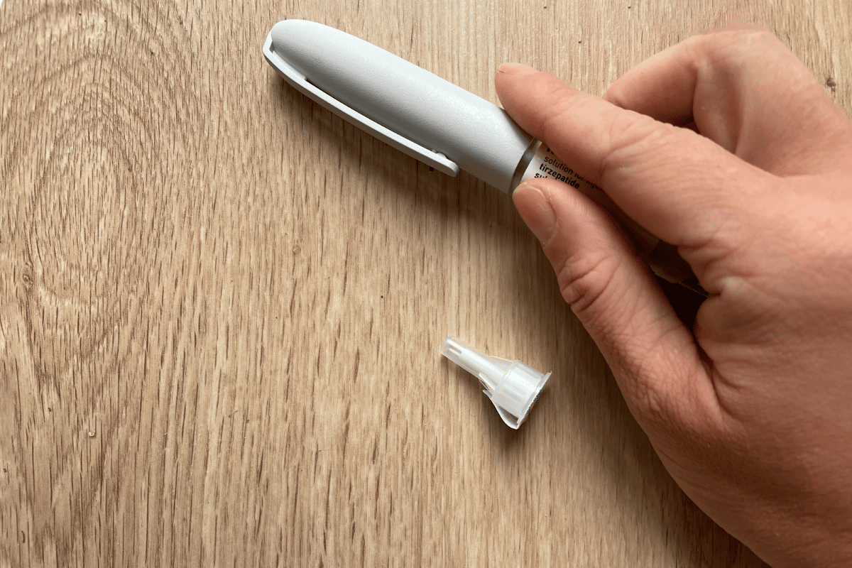 Hand Holding Tirzepatide Injection Pen with Cap on Wooden Surfac
