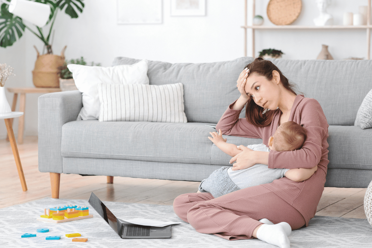 Motherhood Exhaustion. Tired mom breastfeeding baby and working on laptop at home