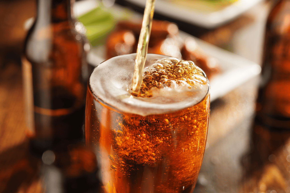 Pouring beer into glass with bbqchicken wings in background